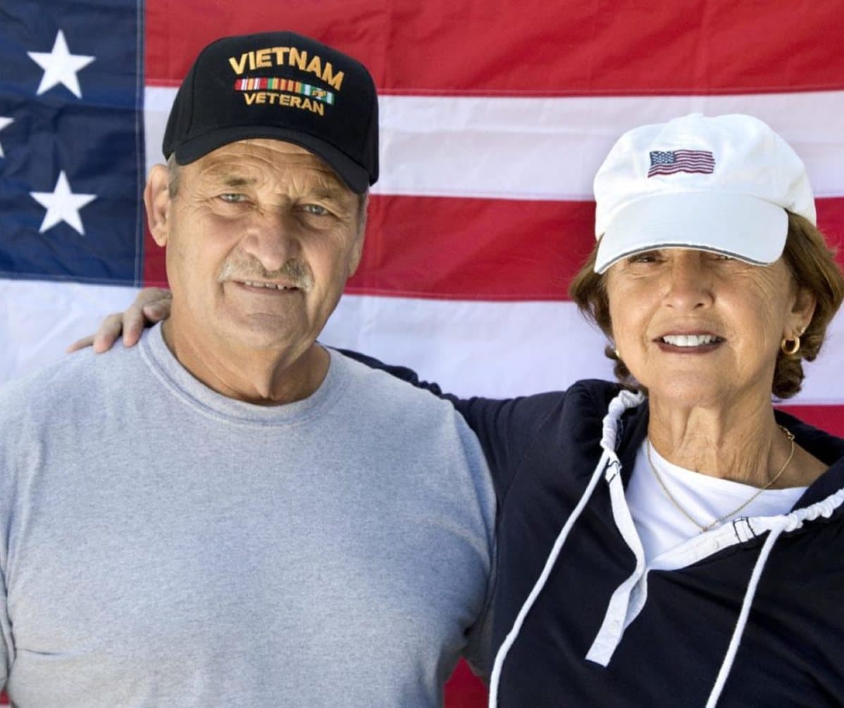 A Veteran and his wife standing in front of an American flag
